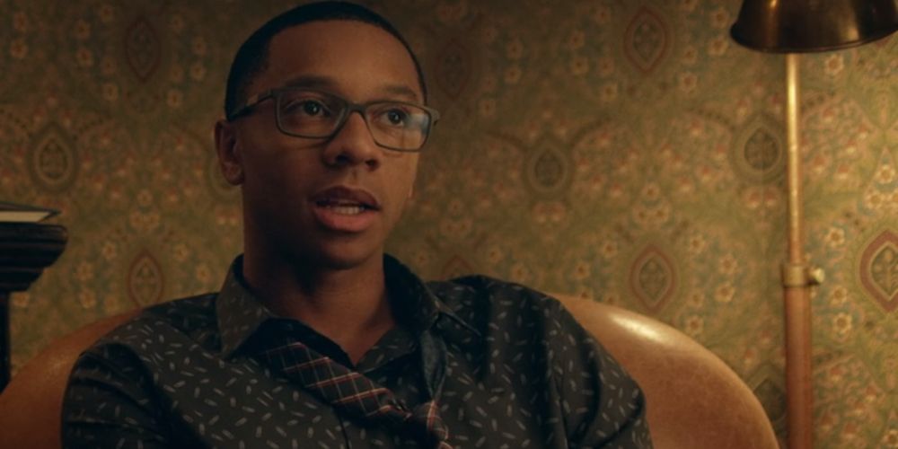 Lionel wears a silk shirt and tie while sitting on a chair in Dear White People