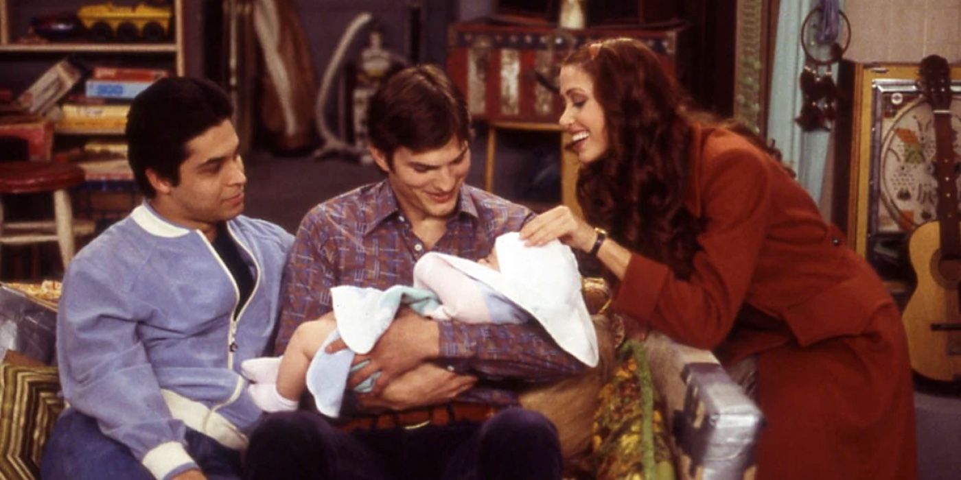 Michael holding his daughter Betsy in That 70s Show while Fez and Brooke look on