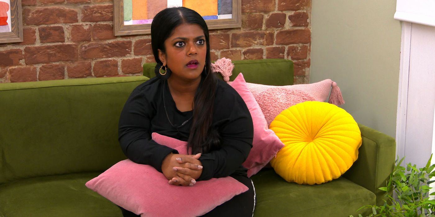 Ruksana from The Circle season 3, sitting on the couch looking shocked.