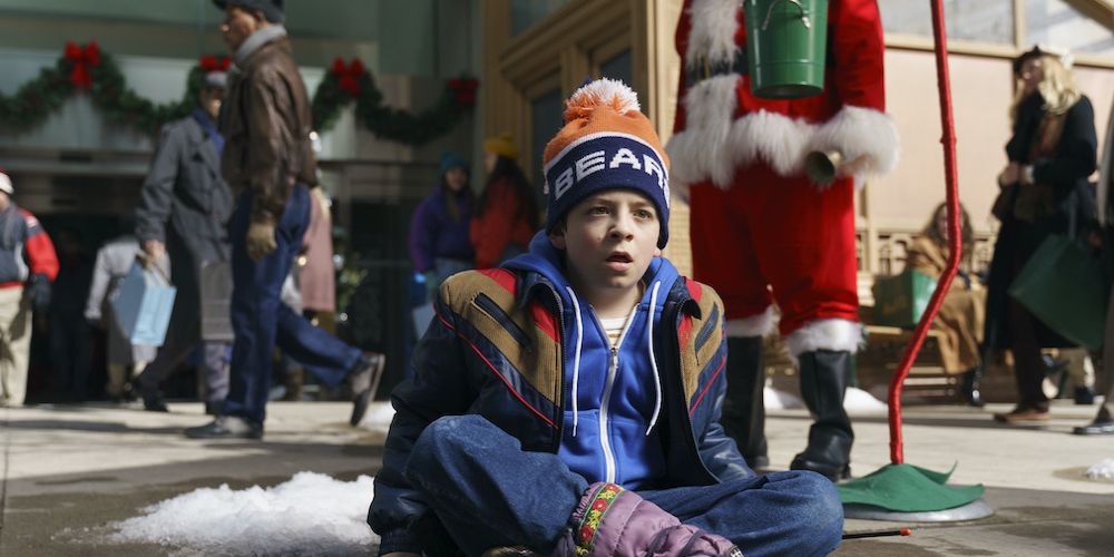 Jake está sentado no chão do lado de fora de uma loja no 8-Bit Christmas.