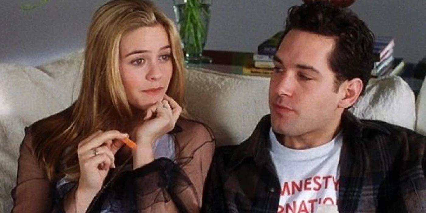 Alicia Silverstone sits next to Paul Rudd as they both look on from Clueless