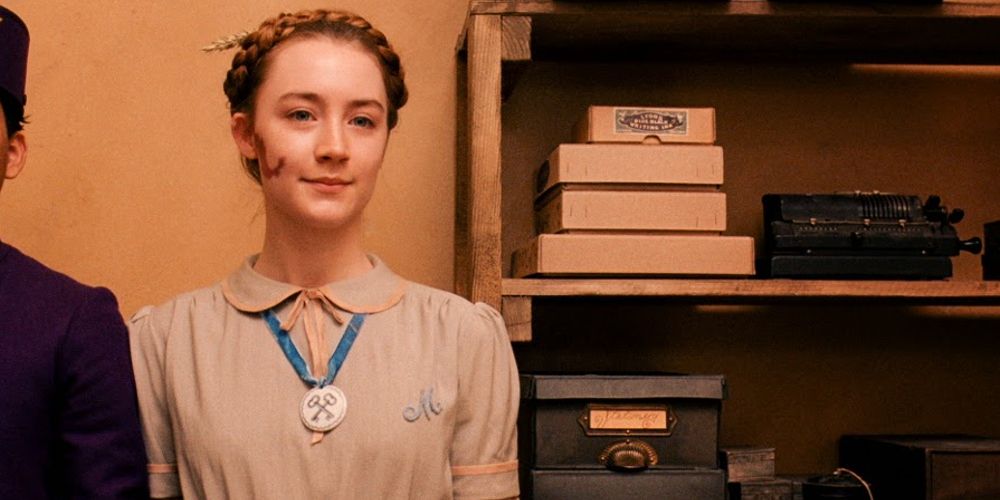 Agatha smiles sweetly standing next to Zero in The Grand Budapest Hotel.