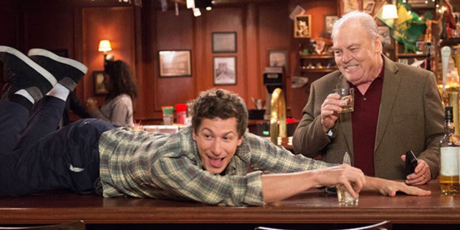 Jake lying on a bar top while Jimmy Brogan stands next to him in Brooklyn Nine-Nine