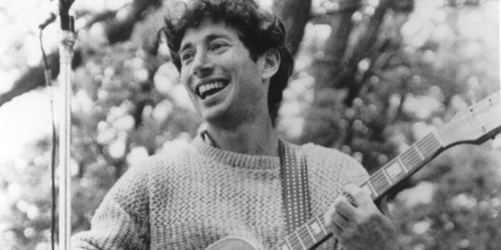 A grinning Jonathan Richman plays guitar and sings on stage.
