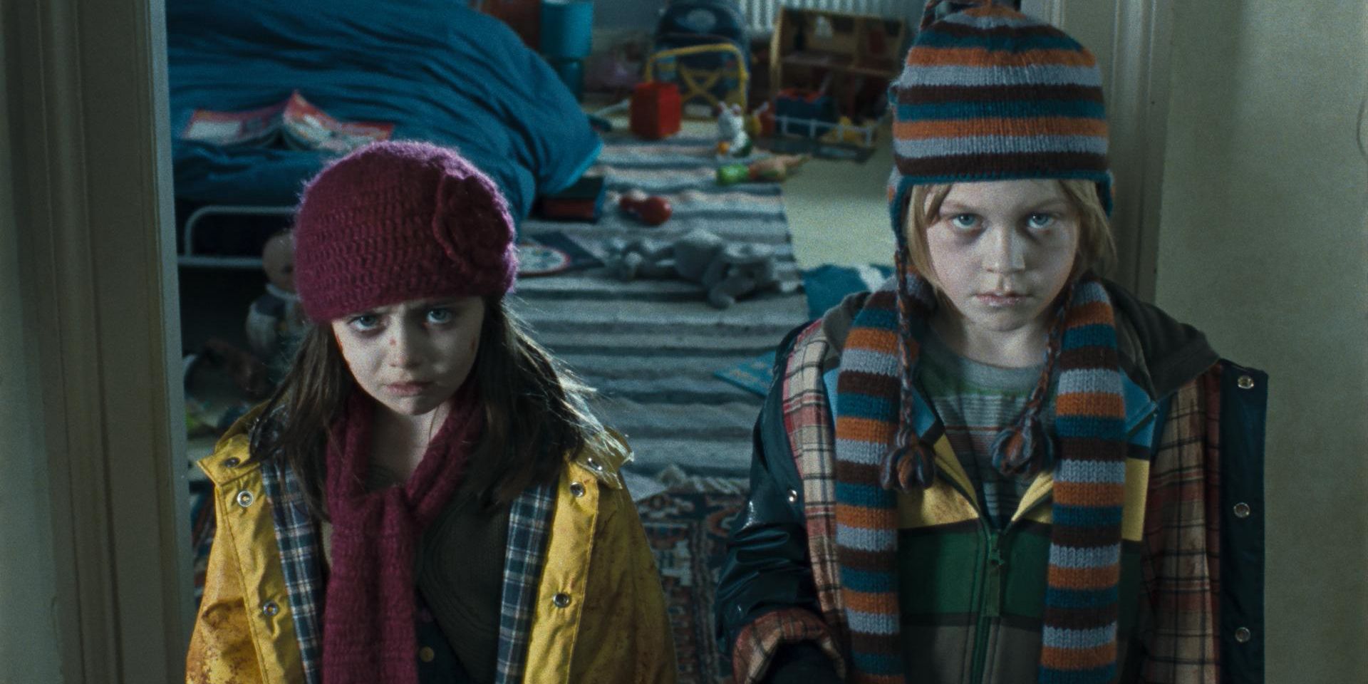 Two of the killer kids in The Children stand in a doorway with the scarves and hats on