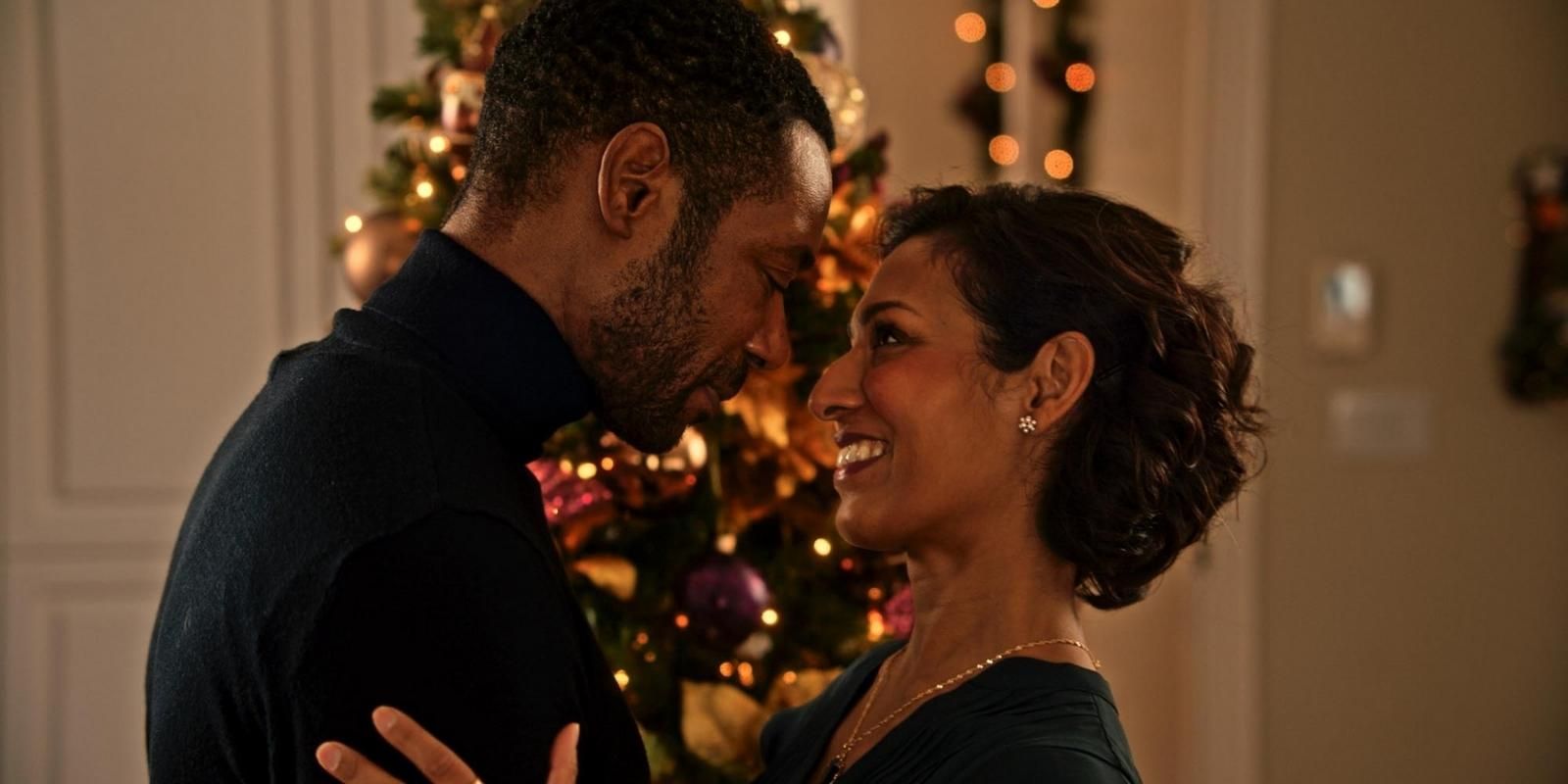 Rekha Sharma and Dion Johnstone embrace and smile in front of a Christmas tree in Baking Spirits Bright