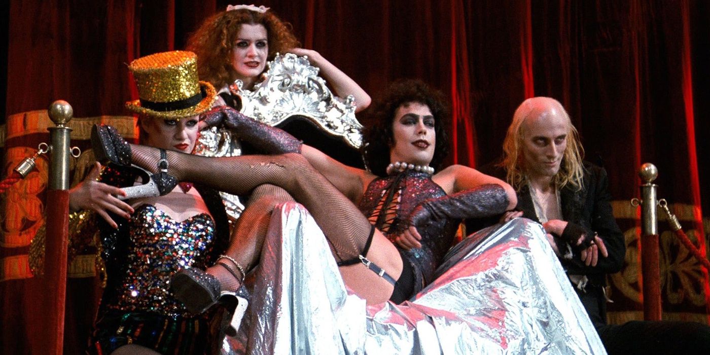 Frank-N-Furter lounges in a chair with others in the cast around in The Rocky Horror Picture Show