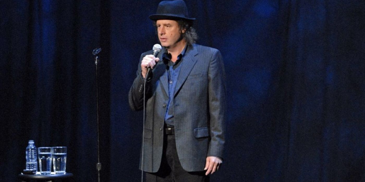 Comedian Steven Wright holding a microphone on stage