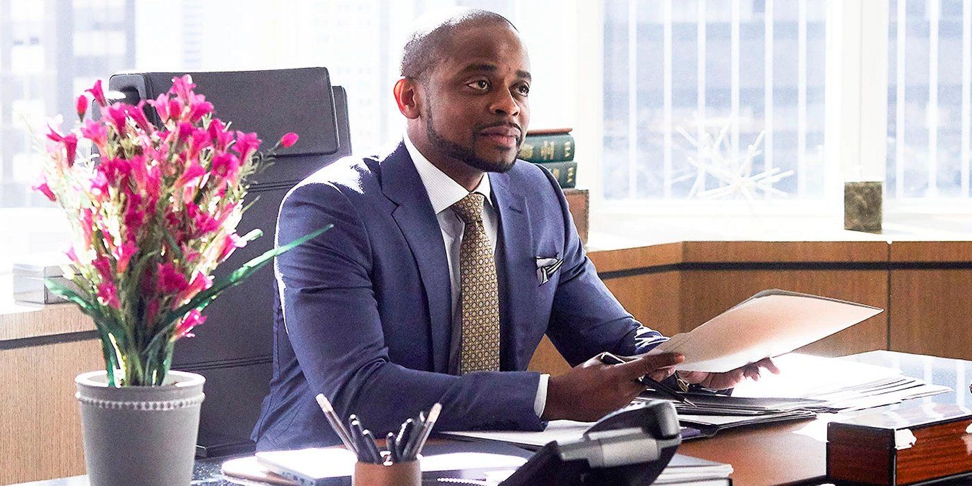 Due Hill sitting behind a desk wearing a suit in an episode of Suits.