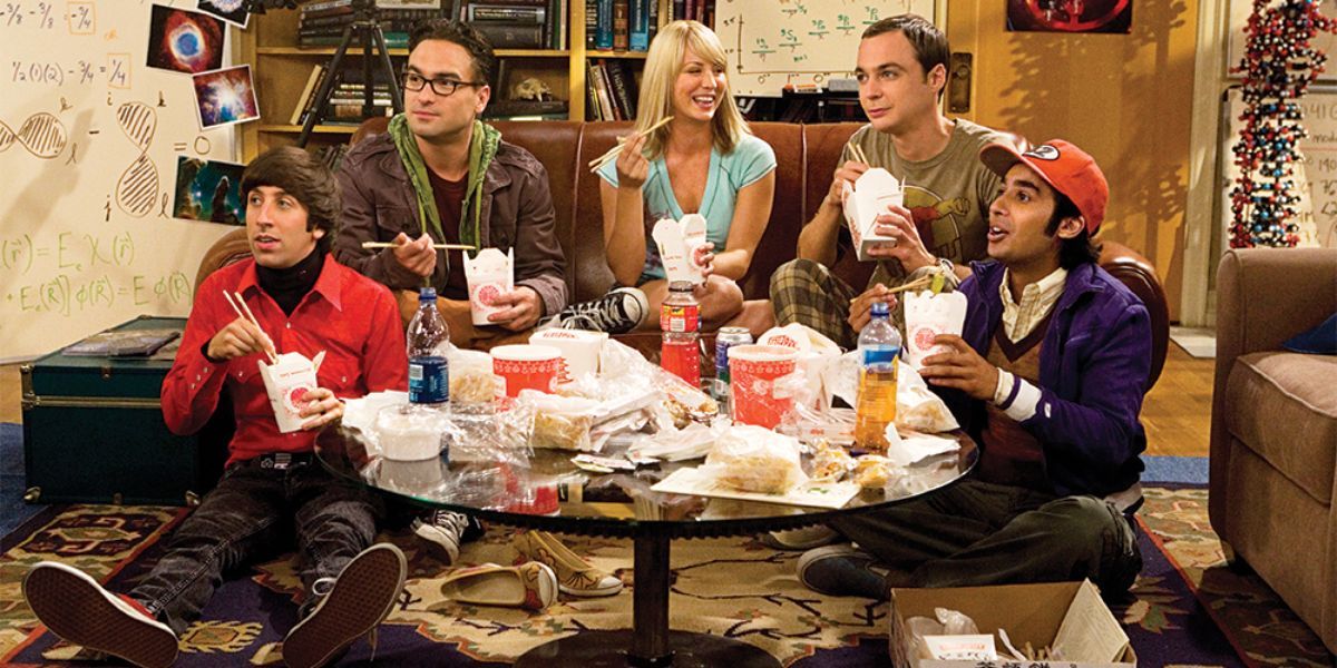 Penny, Leonard, Sheldon, Howard e Raj sentados e comendo no apartamento 4A em TBBT