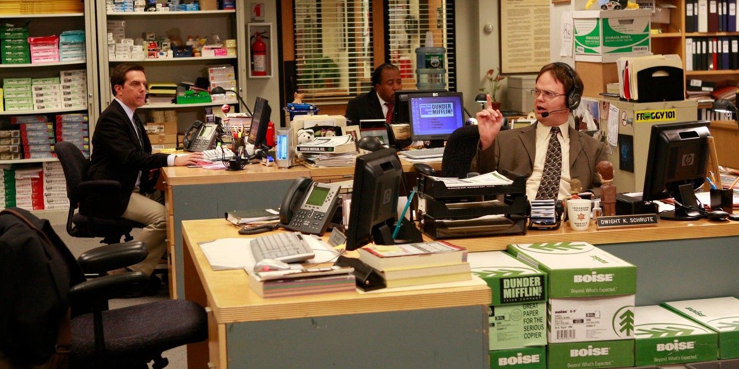 The cubicles of The Office set and Dwight on the phone and Andy and Stanley watch