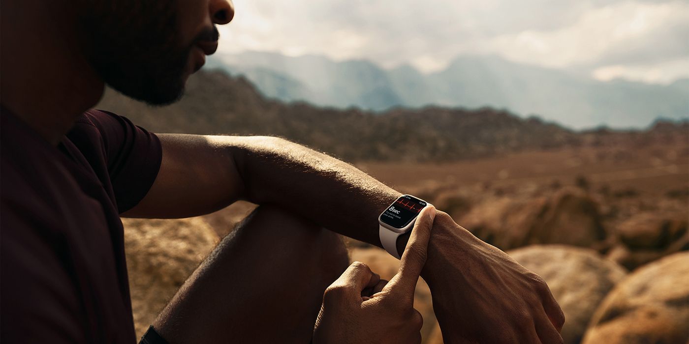A man sitting outdoors wearing an Apple Watch Series 7 and taking an ECG measurement.