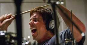 Christian Bale as Michael Burry wearing headphones, screaming, and banging on drums in a scene from The Big Short.