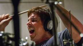 Christian Bale as Michael Burry wearing headphones, screaming, and banging on drums in a scene from The Big Short.