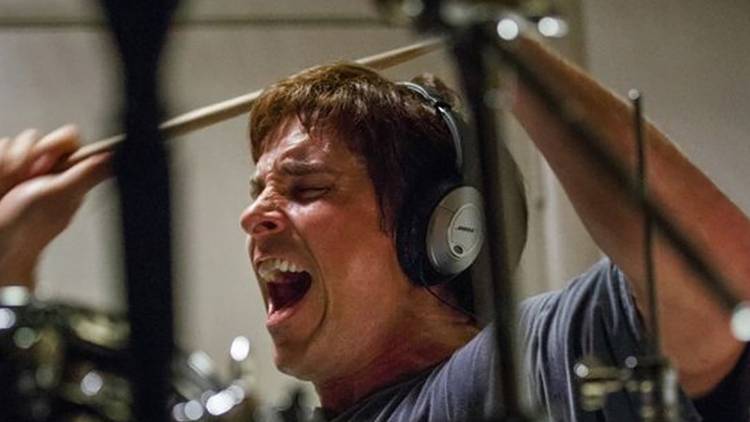 Christian Bale as Michael Burry wearing headphones, screaming, and banging on drums in a scene from The Big Short.
