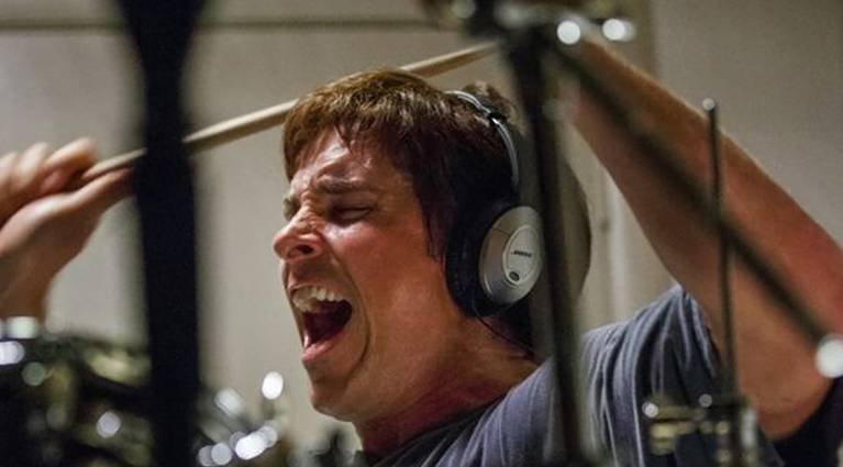 Christian Bale as Michael Burry wearing headphones, screaming, and banging on drums in a scene from The Big Short.