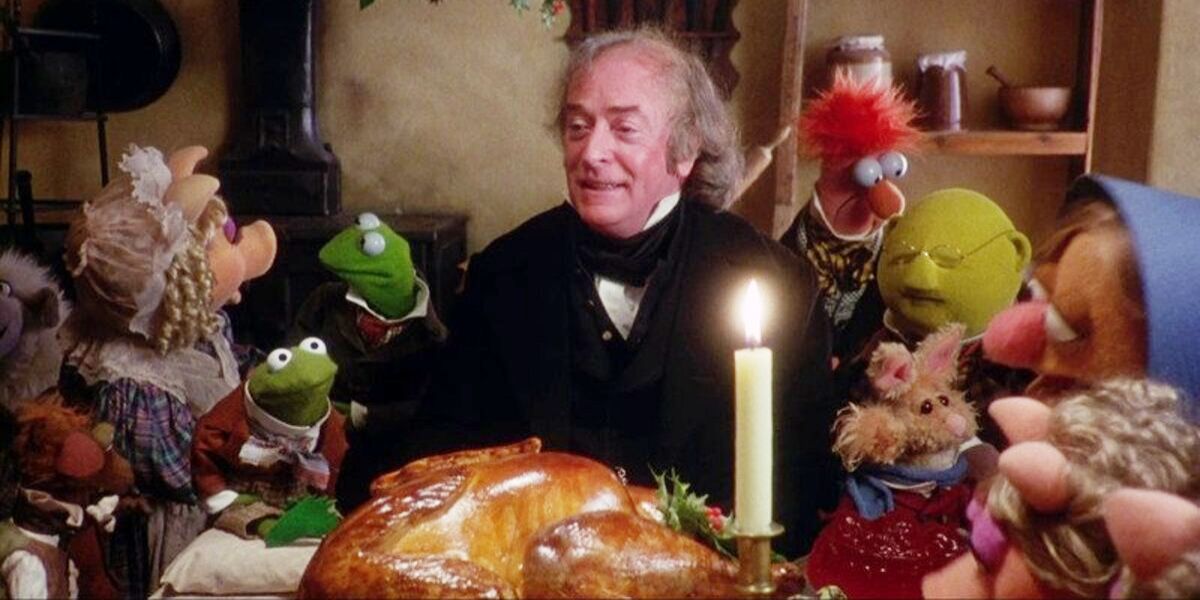 Scrooge sits at a table with food and guests in The Muppet Christmas Carol.