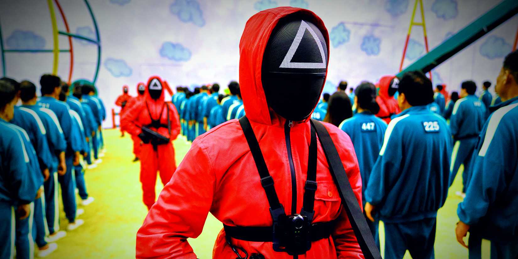 A line of guards standing with guns next to the contestants in Squid Game