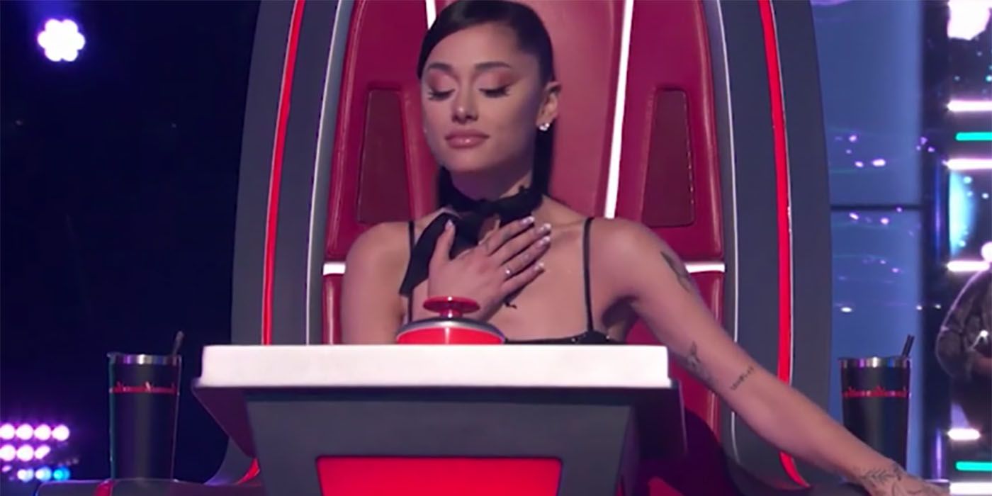 Ariana Grande sitting in her chair on The Voice, eyes closed, hand on her chest.