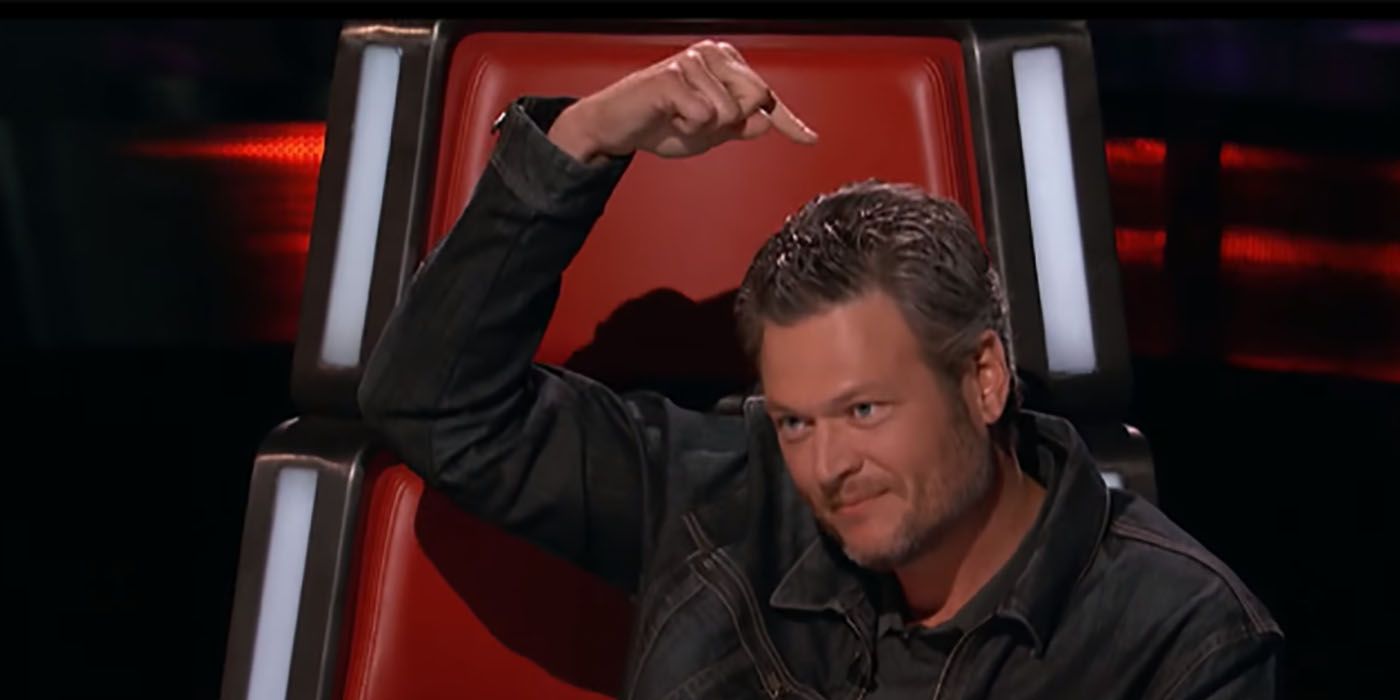 Blake Shelton sitting in his chair on The Voice, pointing his finger at the top of his head.
