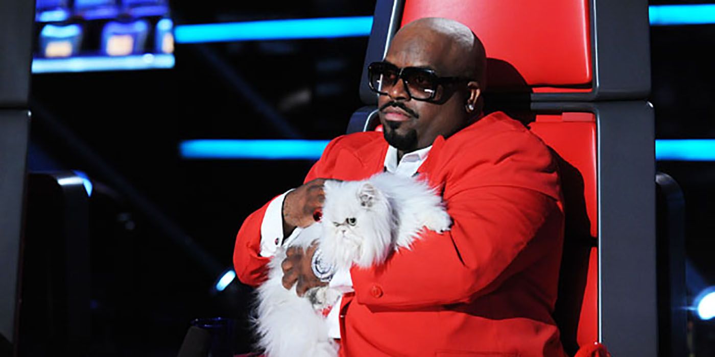 CeeLo Green sitting in his chair on The Voice, holding a white cat.