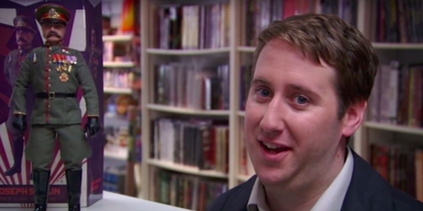 Close-up of Gerard speaking in front of book shelves in Peep Show