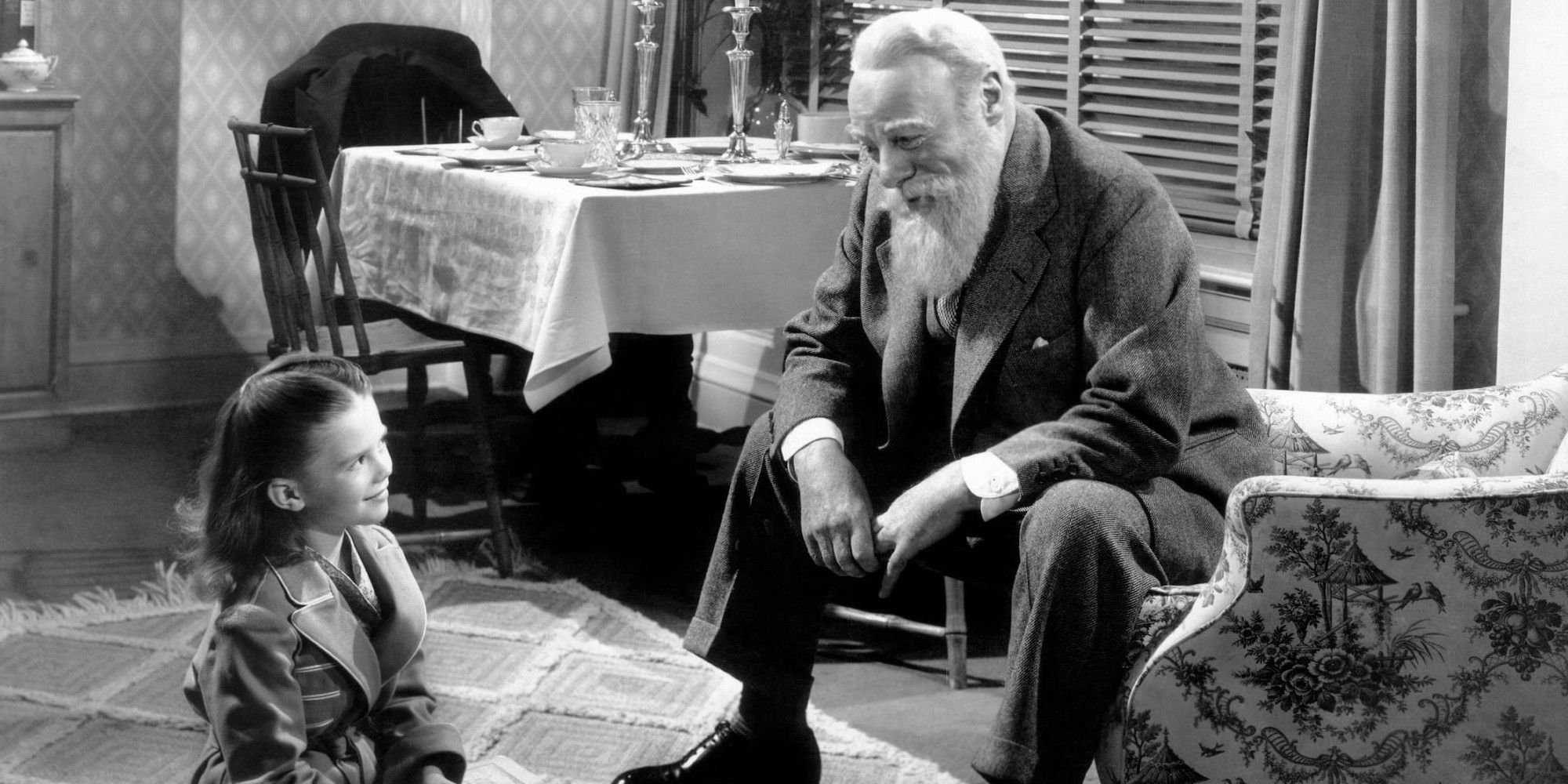 Kris sits in a chair and Suzie sits on the floor in Miracle on 34th Street