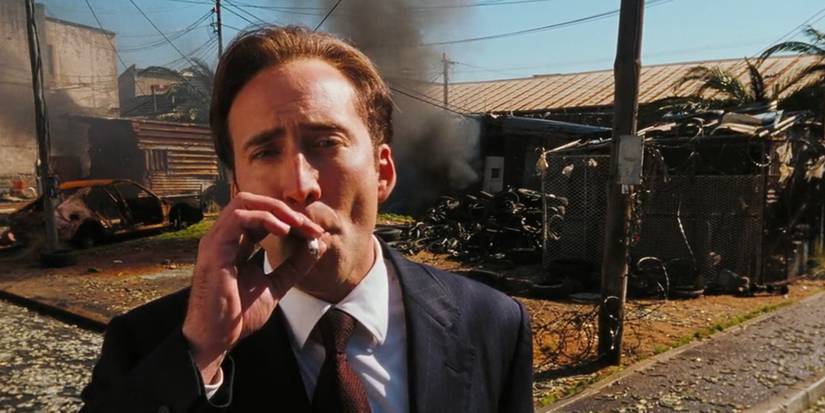 Nicolas Cage as Yuri Orlov smokes a cigarette while standing in front of smoking wreckage in Lord of War