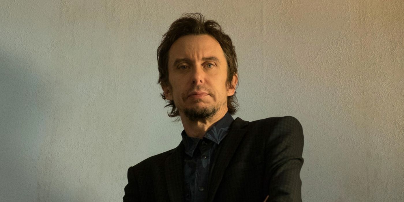 Super Hans looks stoic standing in front of a blank wall in Peep Show