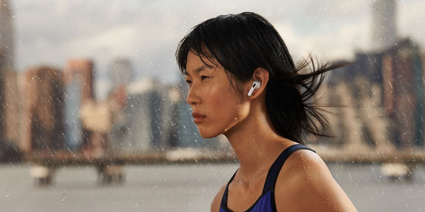 A woman walking in the rain with a pair of the Apple AirPods Pro in her ears, a cityscape in the distance.