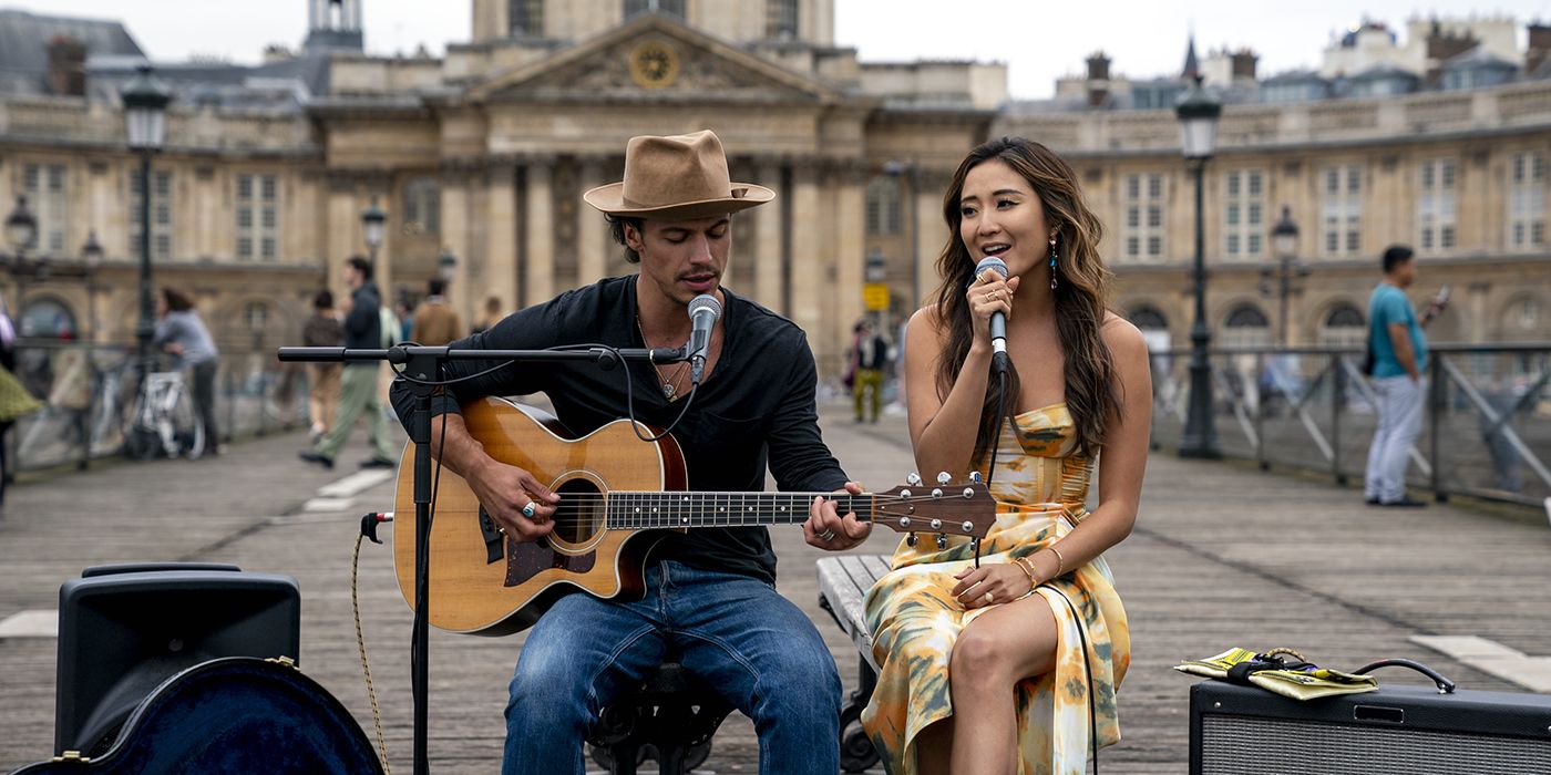 Benoit and Mindy on the street, him playing guitar, her singing in Emily in Paris.