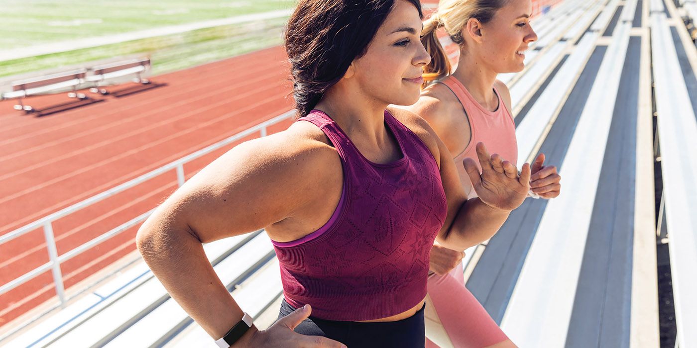 Two women running on a track wearing the Fitbit Inspire 2 activity tracker.