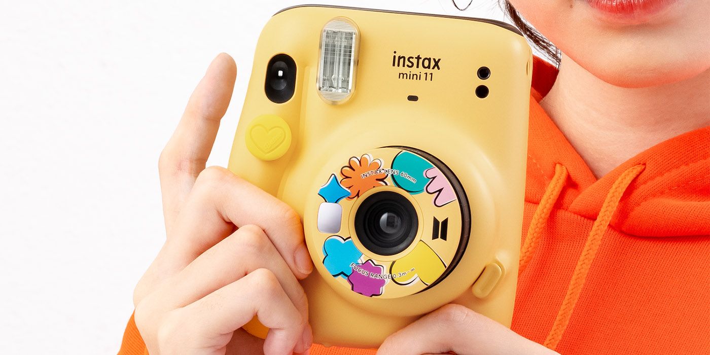 A hand holding the Fujifilm Instax Mini Butter edition instant camera.