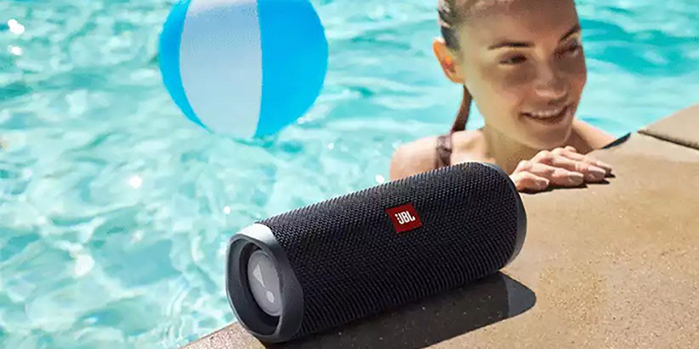 JBL Flip 5 portable Bluetooth speaker sitting on the edge of a pool, a woman beside it.