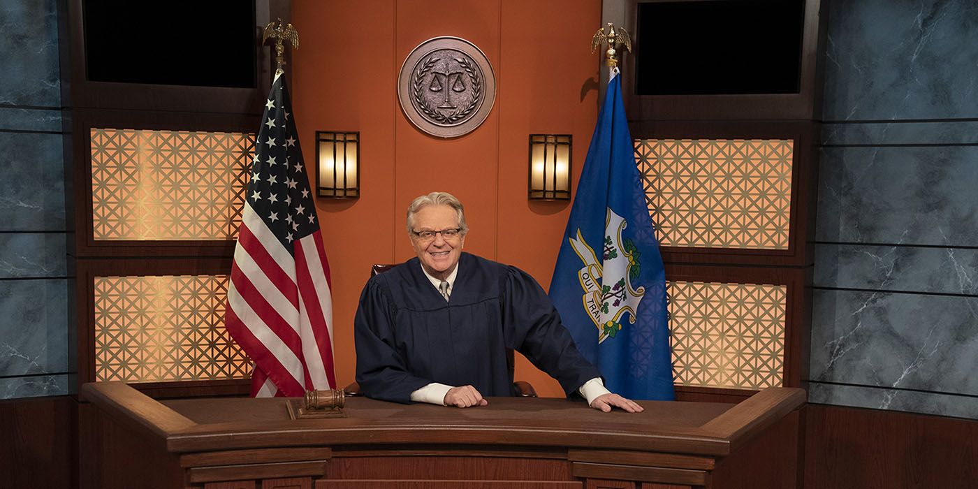 Jerry Springer sitting behind a judge&rsquo;s bench with a robe in a scene from Judge Jerry.