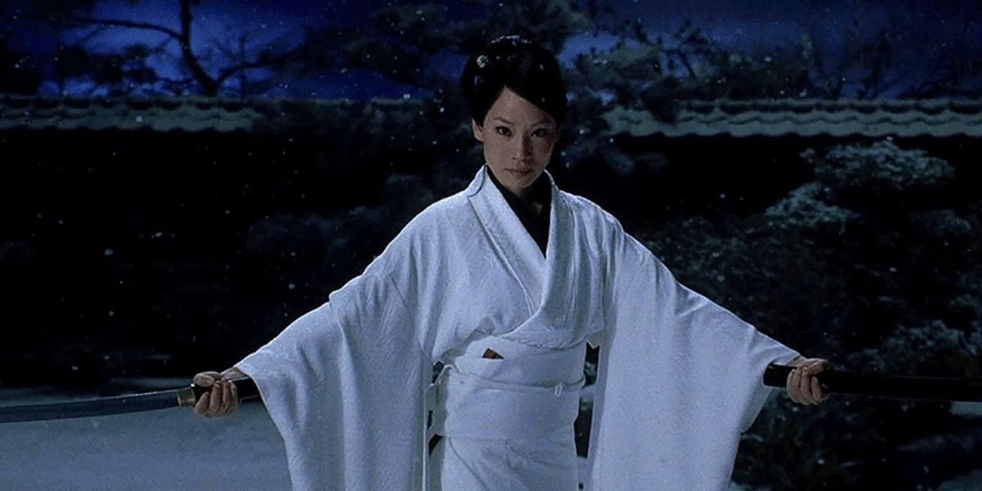 Lucy Liu in a white robe with her hands outstretched, swords in either one in a scene from Kill Bill.