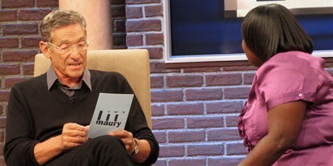 Maury Povich holding a piece of paper reading something with a guest sitting across from him on The Maury Povich Show.