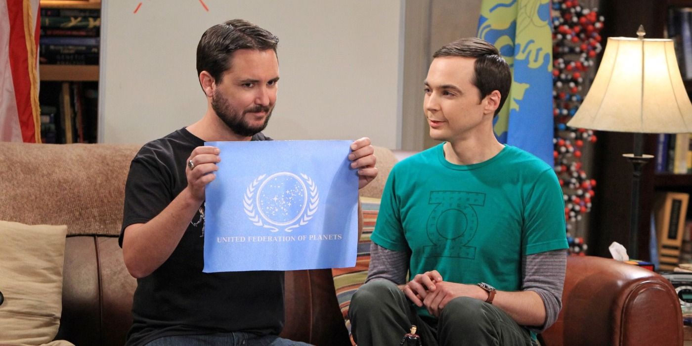 Wil Wheaton senta ao lado de Sheldon segurando uma bandeira no TBBT