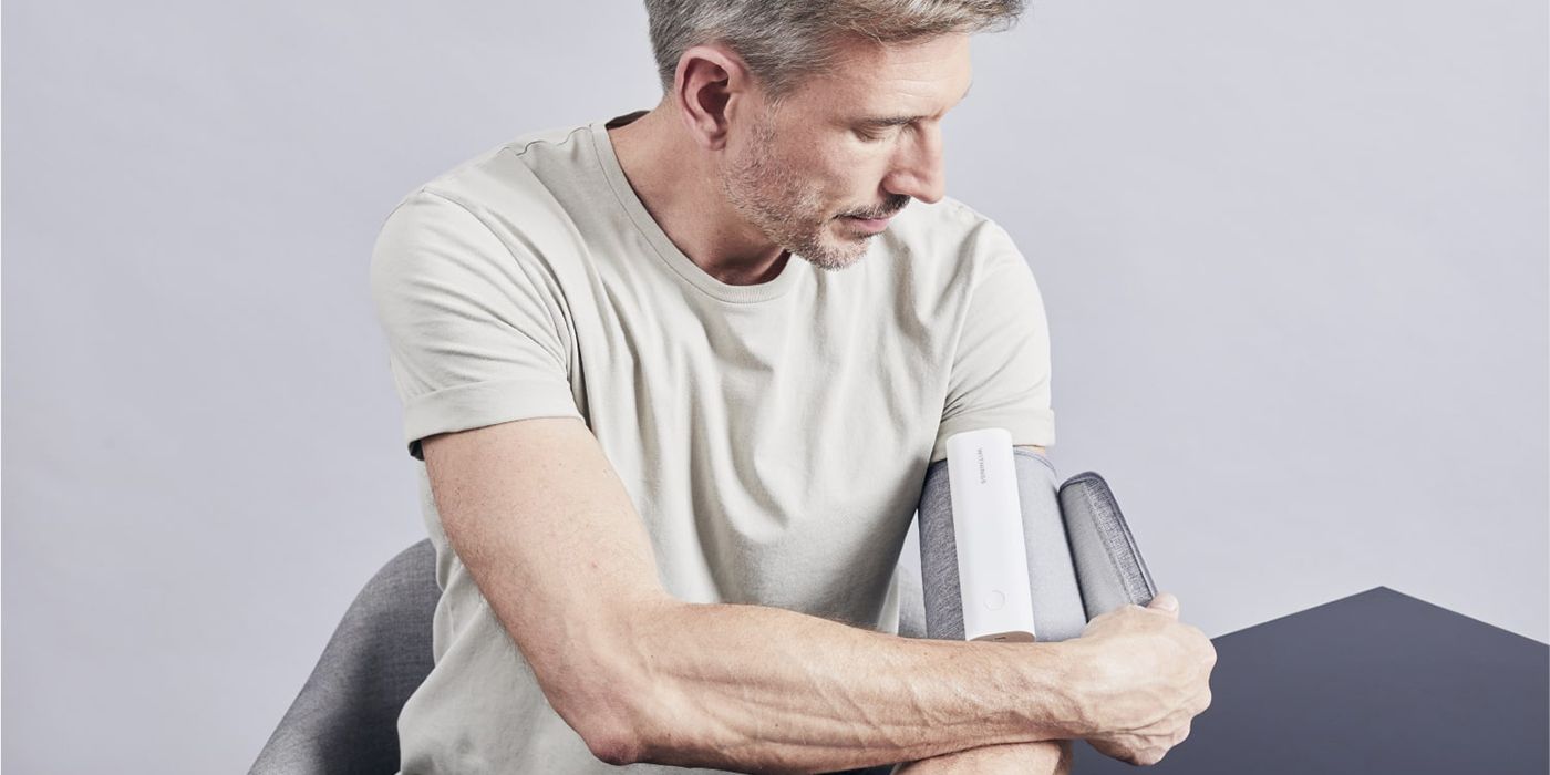 A white-haired man wearing the Withings BP Connect smart blood pressure monitor, unraveling it from his arm.