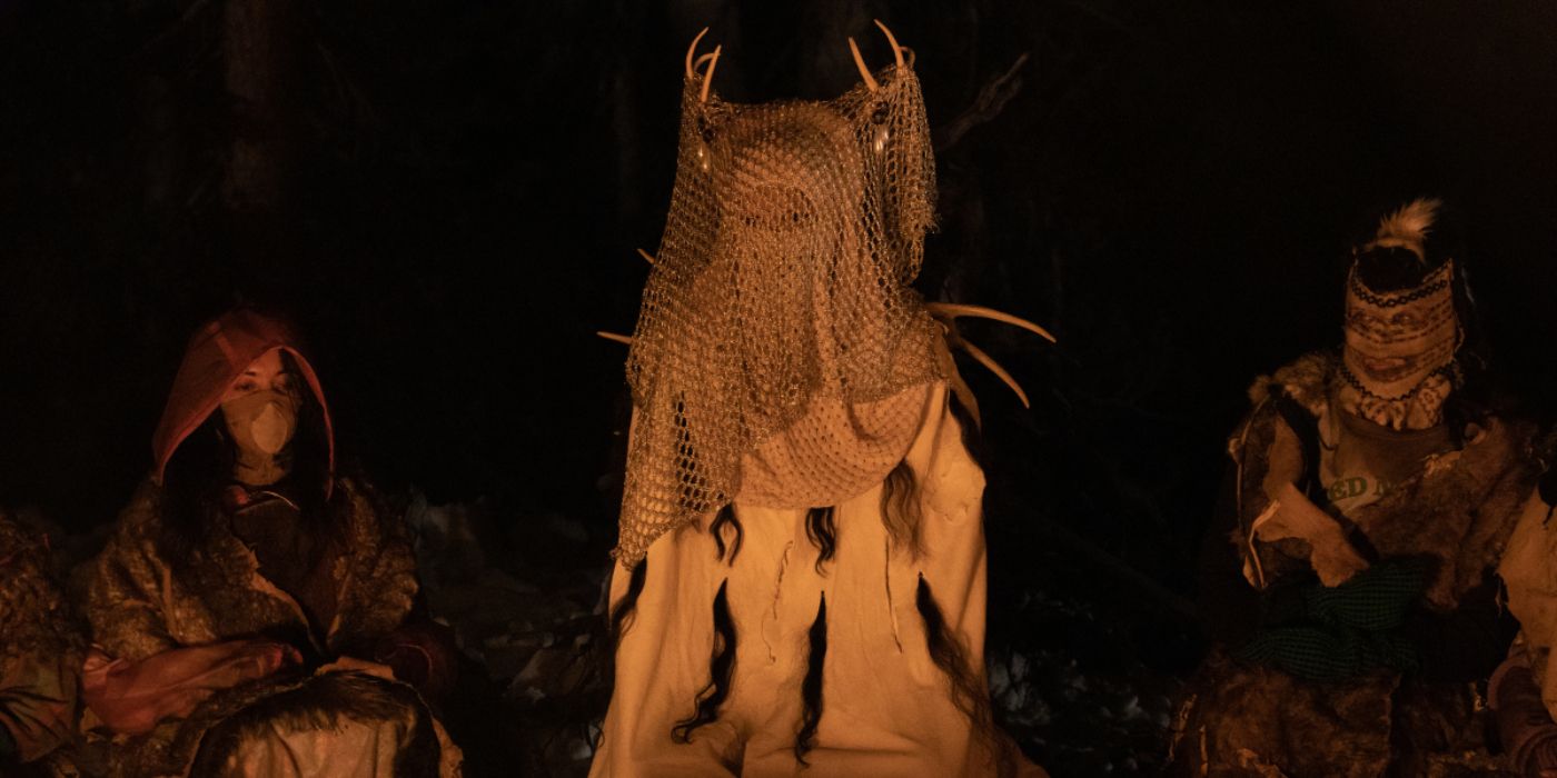 Antler Queen sitting next to two masked characters in Yellowjackets.