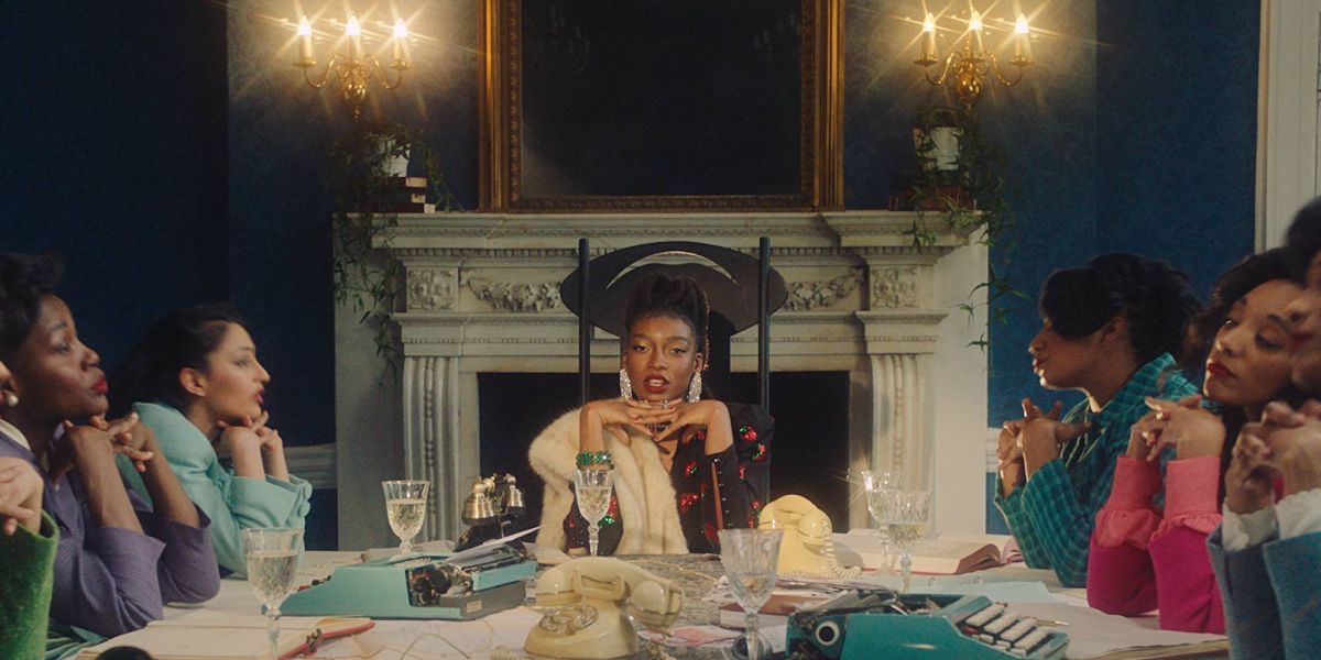 Little Simz sits at a table with other women in the video for Woman