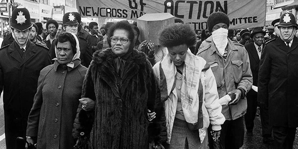 Protesters marching on a street while police officials walk behind them in Uprising