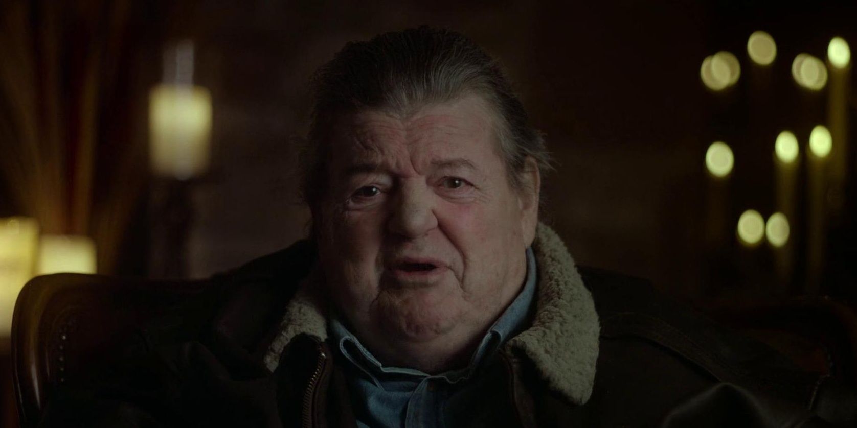 Robbie Coltrane is sitting in front of a candle-lit background at Hogwarts.