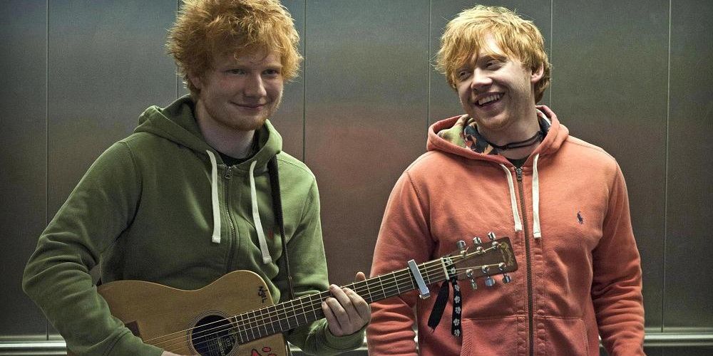 Rupert Grint smiling at Ed Sheeran holding a guitar in Lego House's music video