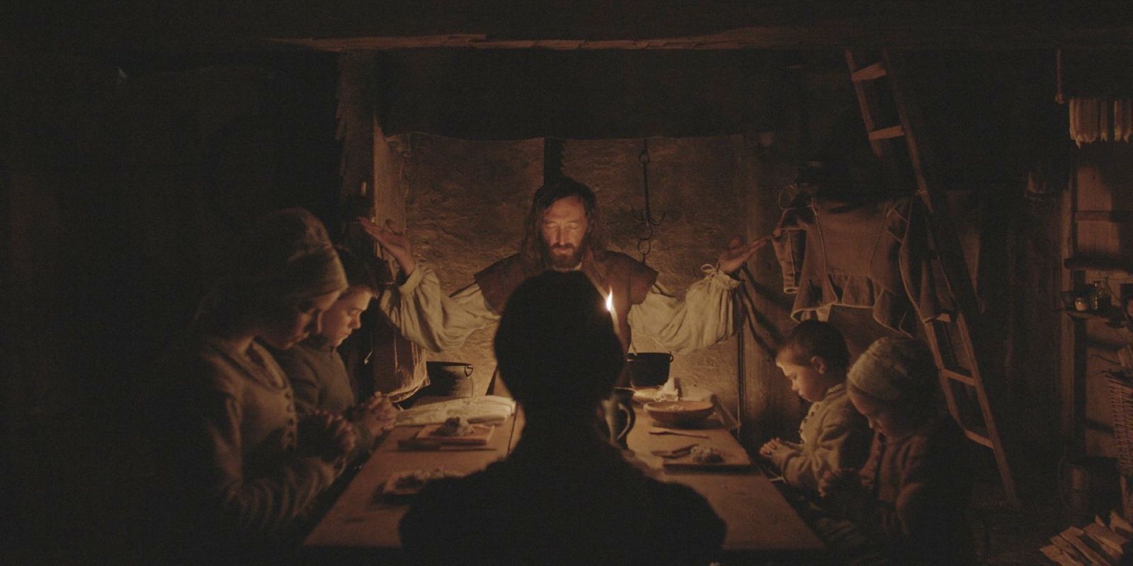 William (Ralph Ineson) reza da cabeceira da mesa em um still do filme de terror de 2015 The Witch