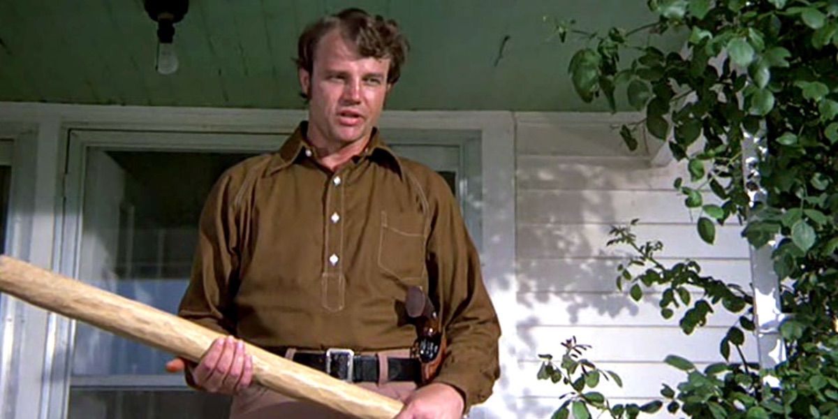 Buford Pusser stands on a porch with a large stick in his hands from Walking Tall
