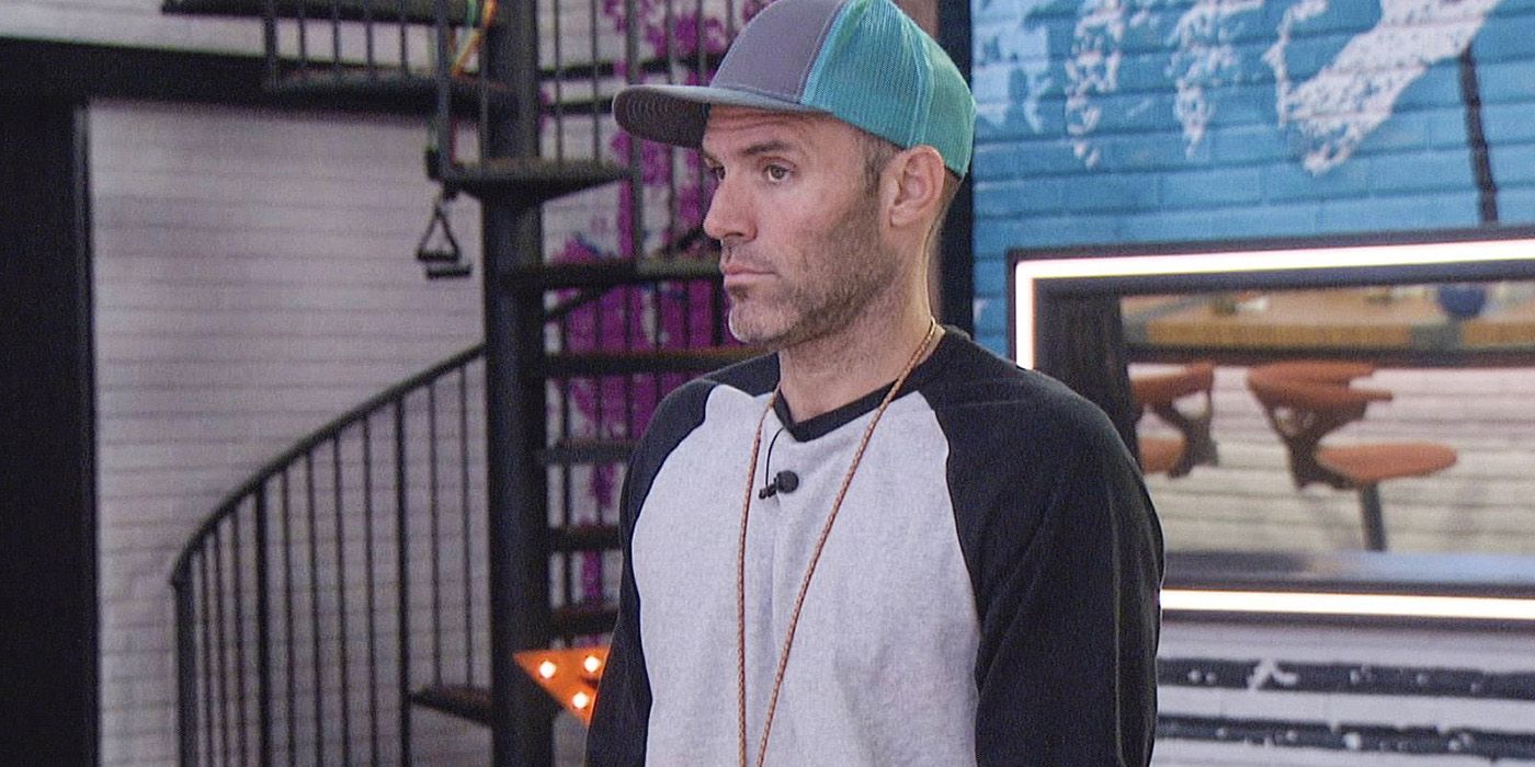 Enzo looking to the side wearing a blue hat and the Veto necklace in a scene from Big Brother.