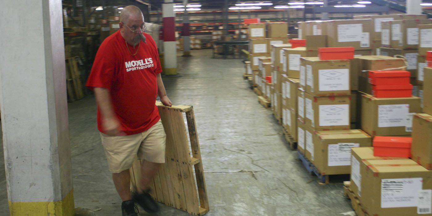 The CEO os Modell's Sporting Goods in disguise, moving boxes in the warehouse in a scene from Undercover Boss.