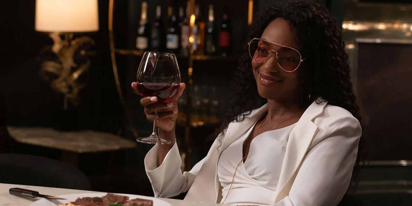 Sloane from Workin' Moms wearing dark glasses, a white suit holding a glass of red wine.