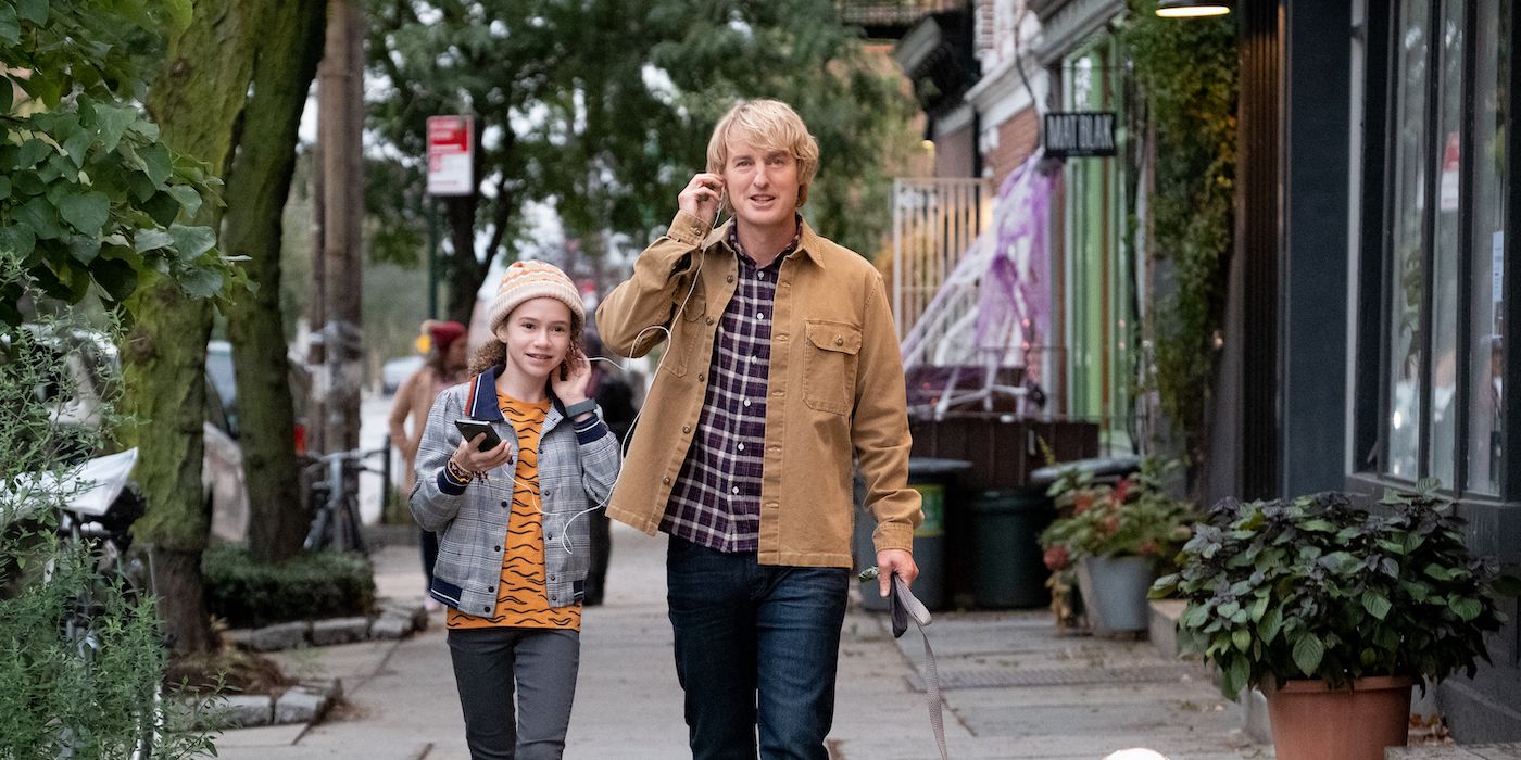 Owen Wilson and Chloe Coleman walk down a street while speaking on cell phones in Marry Me (2022)